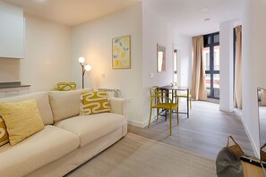 Una sala de estar moderna con un sofá, una mesa de comedor y sillas. Cuenta con una zona de cocina con armarios y una encimera.