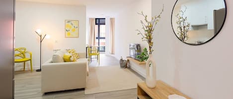 Un salon moderne avec un canapé, un fauteuil jaune, un miroir rond et une petite table sur laquelle est posé un vase.