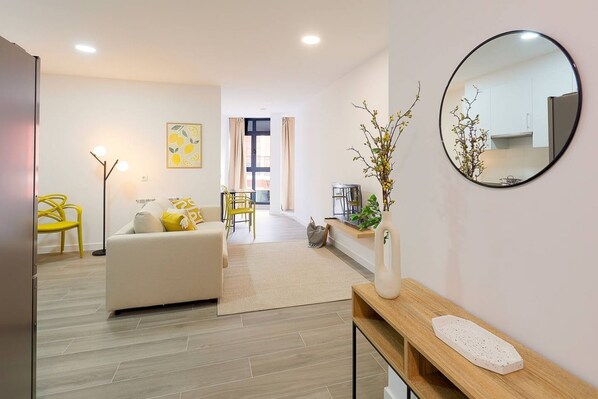 Una sala de estar moderna con un sofá, un sillón amarillo, un espejo redondo y una mesita con un florero.
