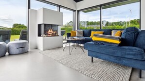 Uma sala de estar moderna com lareira embutida, janelas amplas e um sofá azul com almofadas amarelas.