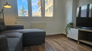 Un salon moderne avec un canapé d’angle, un téléviseur à écran plat, une lampe et une plante en pot.