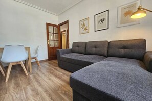 A room with a grey sectional sofa, a white chair, and a wooden door. - 643A moderno apartamento 3 dormitorios (Oviedo)