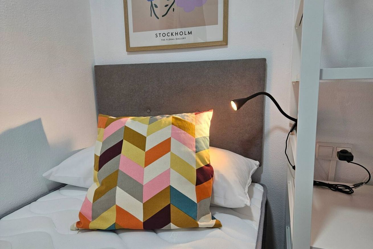 A bed with a colorful chevron-patterned pillow, a framed picture on the wall, and a bedside lamp.