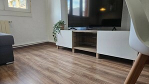 Un salon avec un téléviseur à écran plat posé sur un meuble blanc, une plante en pot et un canapé gris.