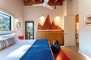 A bedroom with a bed, a blue bench, a wooden cabinet, and a view of the outdoors.
