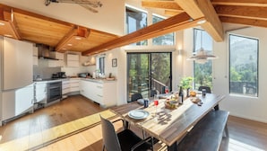 Une cuisine moderne avec des poutres en bois, de grandes fenêtres et un coin repas doté d’une banquette.