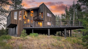 Un chalet rustique doté d’une terrasse, de grandes fenêtres et d’un escalier menant à un niveau supérieur.