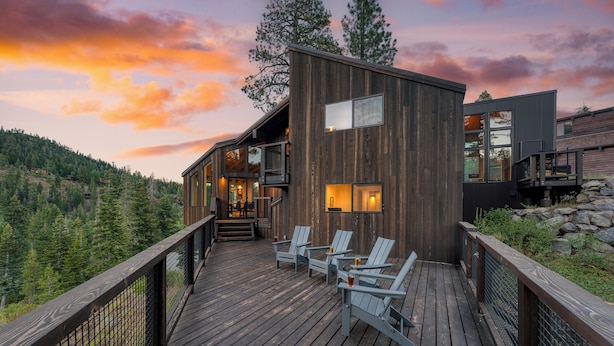 Une maison moderne en bois dotée d’une terrasse, d’un espace salon extérieur et offrant une vue imprenable sur les montagnes.