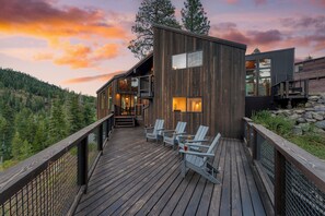 A modern wooden house with a deck, outdoor seating, and a scenic mountain backdrop. - Trapper by AvantStay | A+ Interior Design w/ Sauna (Alpine)