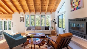 Un salon moderne avec un plafond en bois, de grandes fenêtres, un canapé, une table basse et une cheminée.