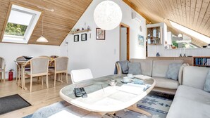 Um loft moderno com teto alto, área de jantar, sala de estar com sofá e mesa de centro, e cozinha com janela com vista para vegetação.