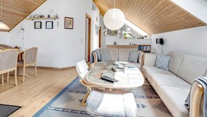 Um amplo loft com teto alto, área de jantar com mesa redonda, sofá e cozinha visível através de uma porta aberta.