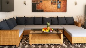 A modern living room with a grey sectional sofa, a wooden coffee table with fruit, and a large abstract painting on the wall. - Villa Inti Seminyak Bali (Seminyak)