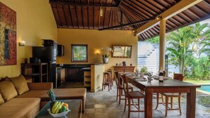 A spacious living area with a dining table, comfortable seating, a kitchen, and a view of the pool. - Villa Inti Seminyak Bali (Seminyak)