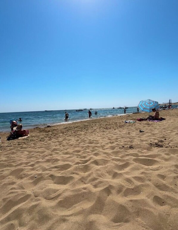 A sandy beach with people and boats in the water, and a clear blue sky. - Via Polonia  (Corfu)