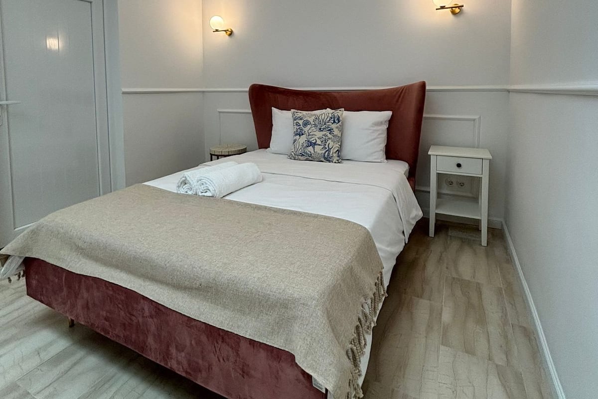 A neatly arranged bedroom with a bed, bedside tables, and wall-mounted lights.