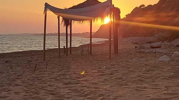Une plage avec une structure recouverte de chaume et un coucher de soleil en arrière-plan.