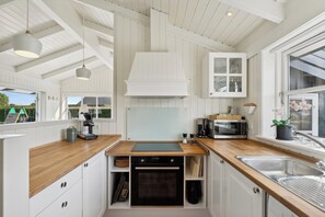Eine moderne Küche mit weißen Schränken, Holzarbeitsplatten, einem eingebauten Backofen, einer Mikrowelle und einem großen Fenster.
