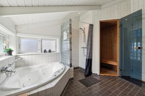 Ein modernes Badezimmer mit einer großen Badewanne, einer Duschkabine aus Glas und einer Holztür.