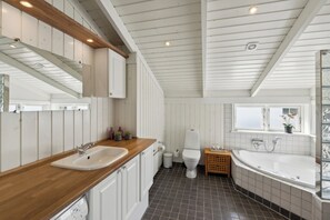 Ein Badezimmer mit einem Holzkosmetikschrank, einer weißen Toilette, einer Badewanne und einem Fenster mit Blick.