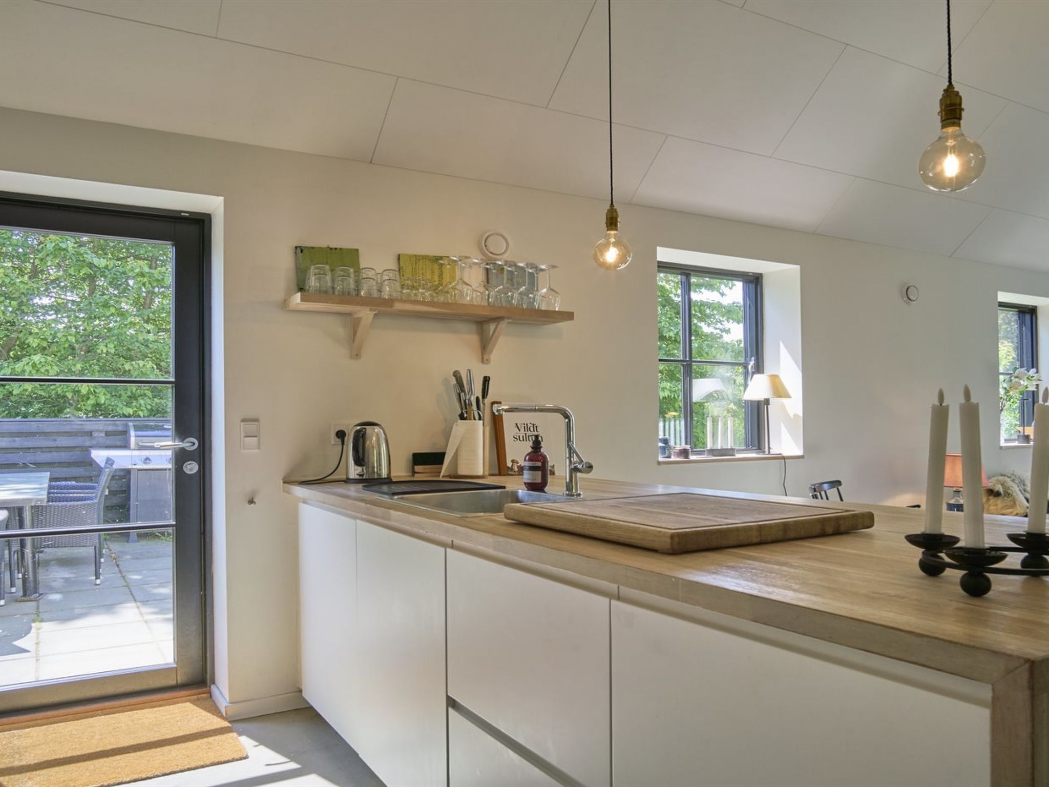 Een moderne keuken met een groot schiereiland, een ingebouwde oven en een raam met uitzicht op een terras.