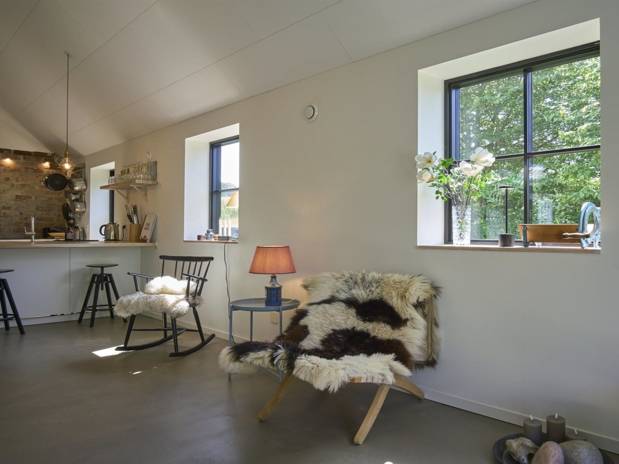 A modern kitchen with a brick wall, a dining area with a fluffy chair, and a large window with a view of trees.