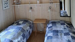 A room with wooden panel walls, two beds with blue and white patterned bedding, a small wooden table, a shelf with decorative items, and a mirror. - Cozy summer house and annex in tranquility (Glesborg)