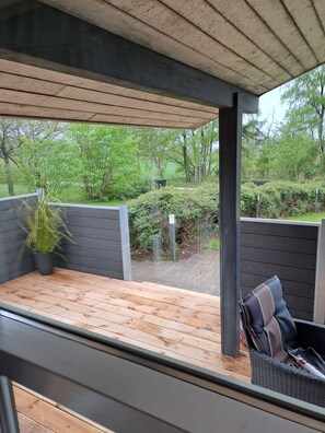 A covered outdoor deck with a wooden floor, a potted plant, and a seating area with a chair and cushions. - Cozy summer house and annex in tranquility (Glesborg)