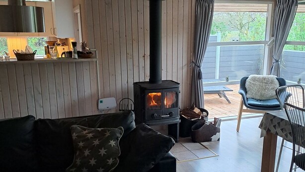 A cozy living room with a black sofa, a table, a fireplace, and a view of the outdoors. - Cozy summer house and annex in tranquility (Glesborg)
