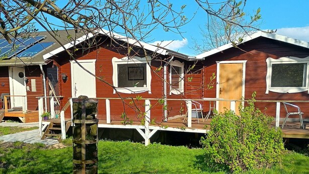 A red wooden cabin with a deck, a small pond, and a stone structure. - Charming summer house in an idyllic area. (Odder Gylling)