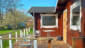 A wooden deck with a table and chairs, a small building with a window, and a wooden fence. - Charming summer house in an idyllic area. (Odder Gylling)