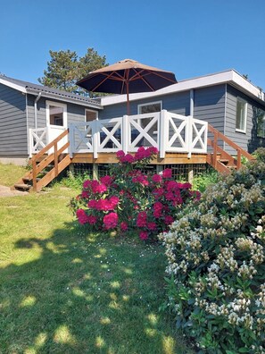 A house with a covered porch, a wooden staircase, and a garden with pink flowers.