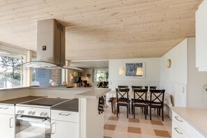 A modern kitchen with a large island, a built-in oven, and a dining area with chairs and a table.