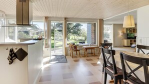 A modern kitchen with a built-in stove, a dining area with a table and chairs, and large sliding glass doors leading to a garden. - Well-located holiday home in Ristinge, Langeland (Humble)