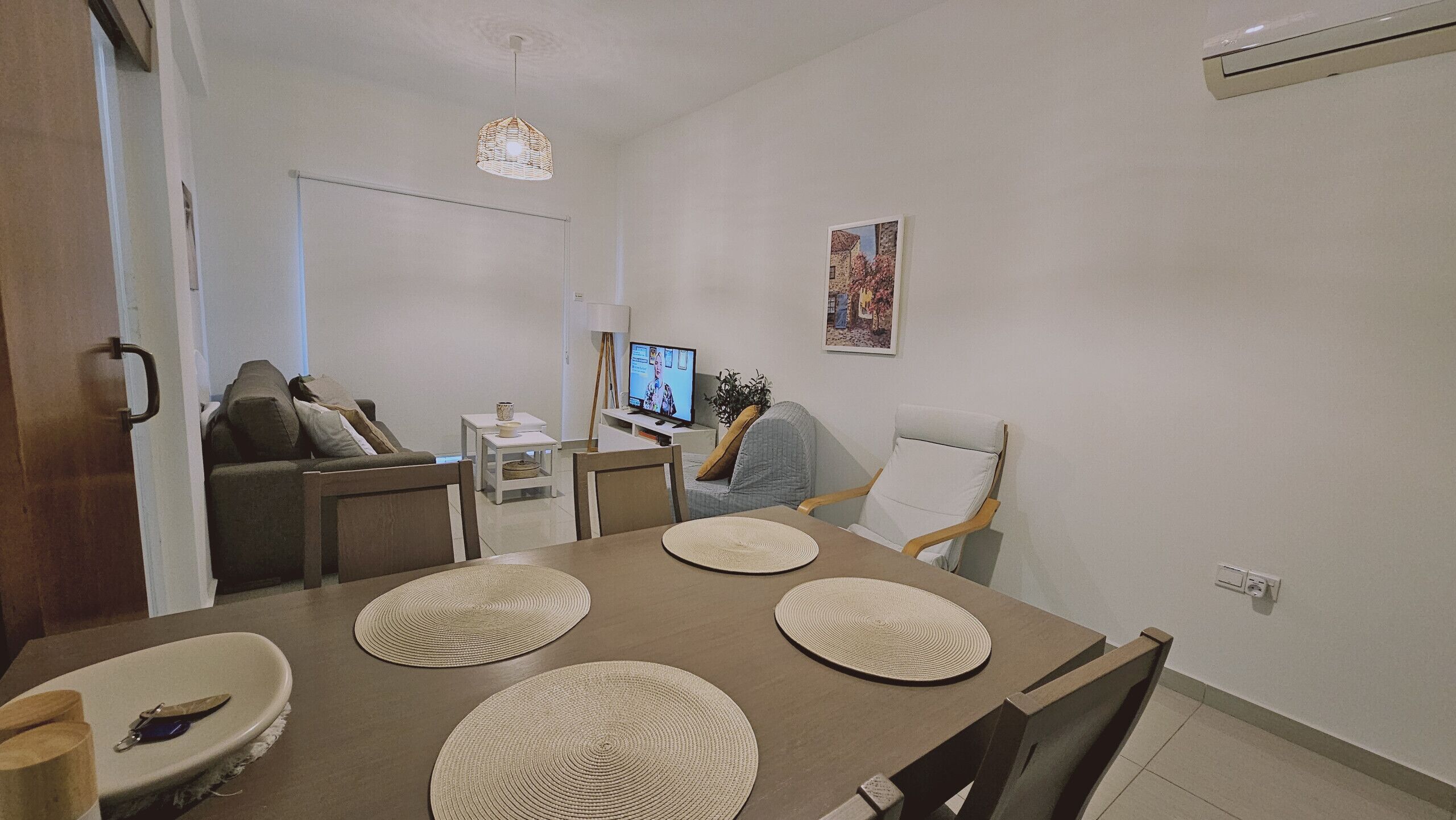 A modern living room with a dining table, sofa, TV, and artwork on the wall.