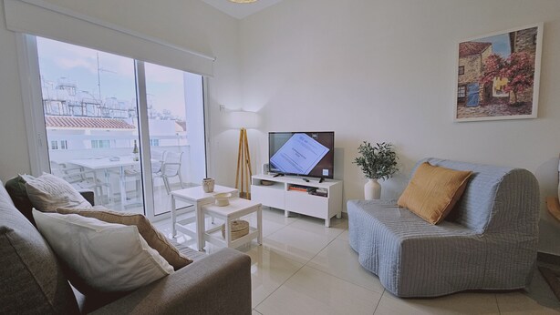 Una sala de estar moderna con un ventanal grande, un televisor de pantalla plana, un sofá, una mesita de centro y un cuadro en la pared.