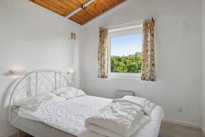 A bedroom with a bed, a window with curtains, a bedside table with a lamp, and a wooden ceiling. - Pool house close to the coast (Vestervig)