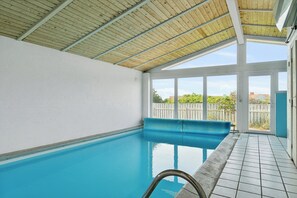 Une piscine intérieure avec un plafond en bois et une vue sur un jardin clos.