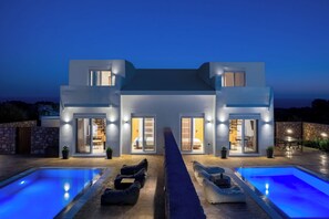 Ein modernes, zweistöckiges Haus mit Swimmingpool, Sitzgelegenheiten im Freien und einem gut beleuchteten Innenraum.
