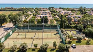 Luftaufnahme eines Wohngebiets mit Tennisplatz, umgeben von Häusern und Grünflächen.