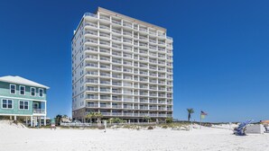 A multi-story hotel with balconies, located on a sandy beach with a clear blue sky. - Royal Palms Condos (Gulf Shores)