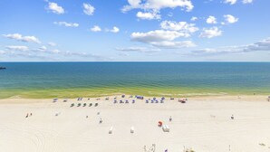 A beach with white sand, clear blue water, and a few umbrellas. - Royal Palms Condos (Gulf Shores)