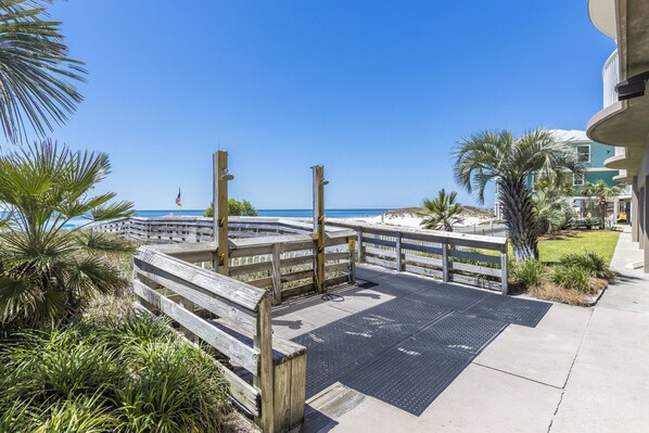 A wooden boardwalk leading to a beach with palm trees and a clear blue sky. - Royal Palms Condos (Gulf Shores)