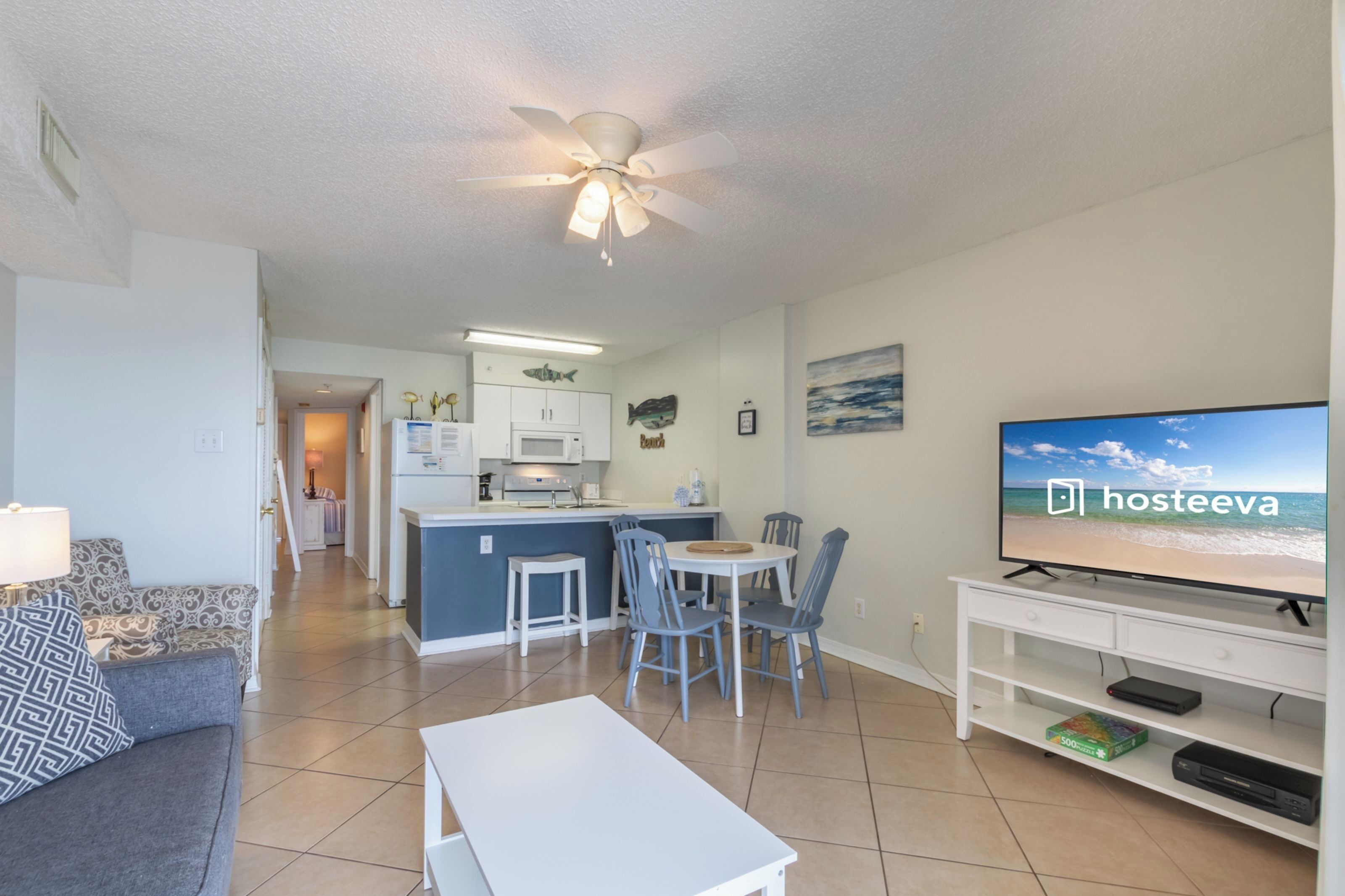 A modern living room with a TV, a dining area, and a kitchen in the background.