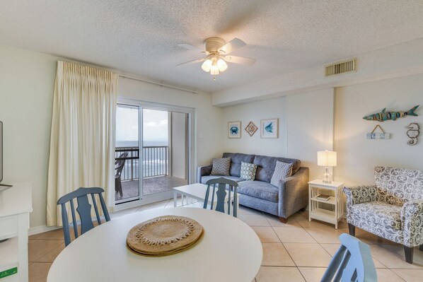 A living room with a sofa, chairs, a dining table, and a ceiling fan. - Royal Palms Condos (Gulf Shores)