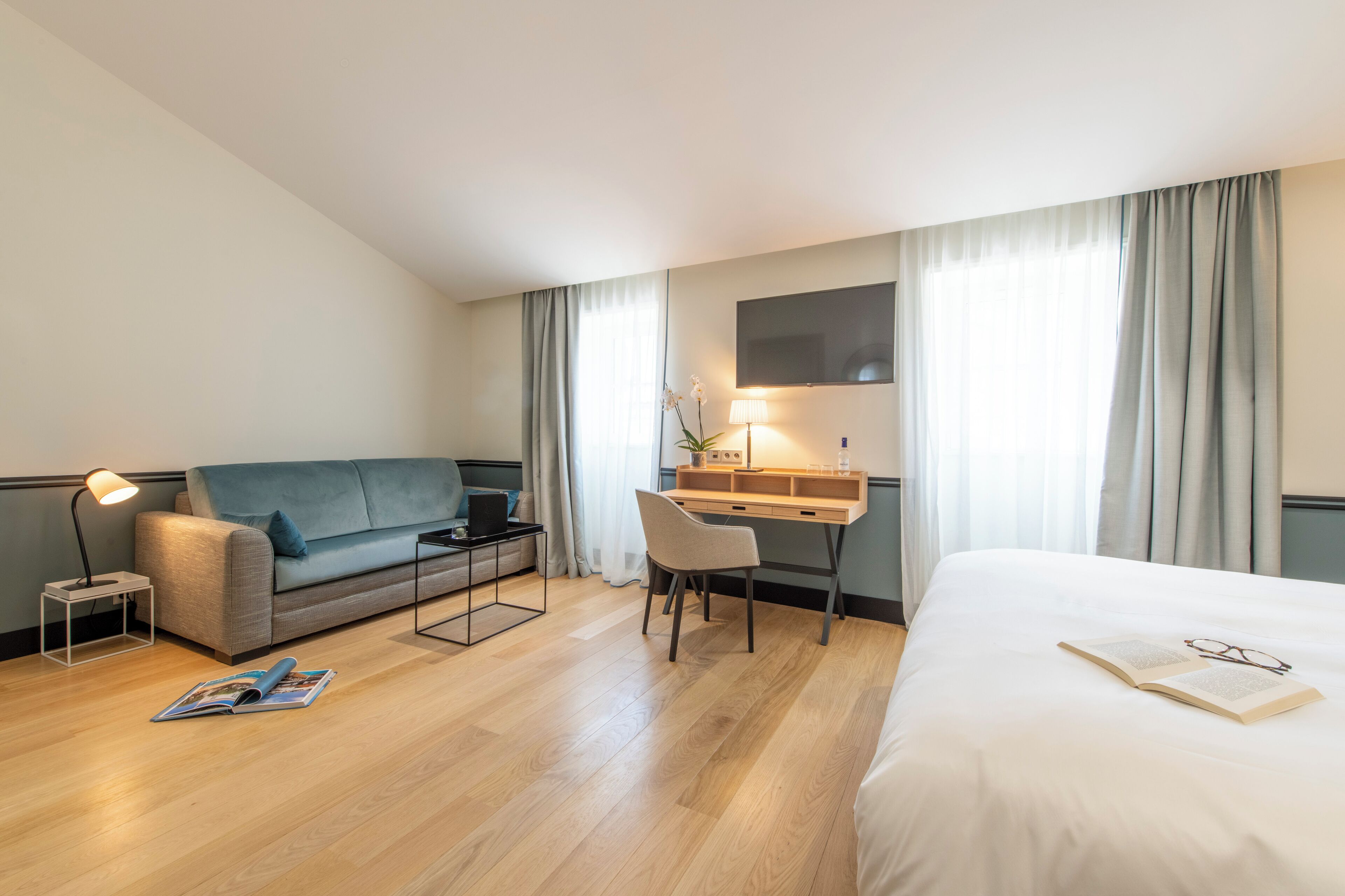 Ein Hotelzimmer mit einem Bett, einem Schreibtisch, einer Couch, einem Sessel, einer Lampe und einem Fernseher.