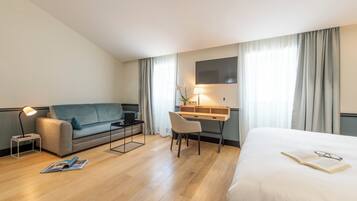 Ein Hotelzimmer mit einem Bett, einem Schreibtisch, einer Couch, einem Sessel, einer Lampe und einem Fernseher.