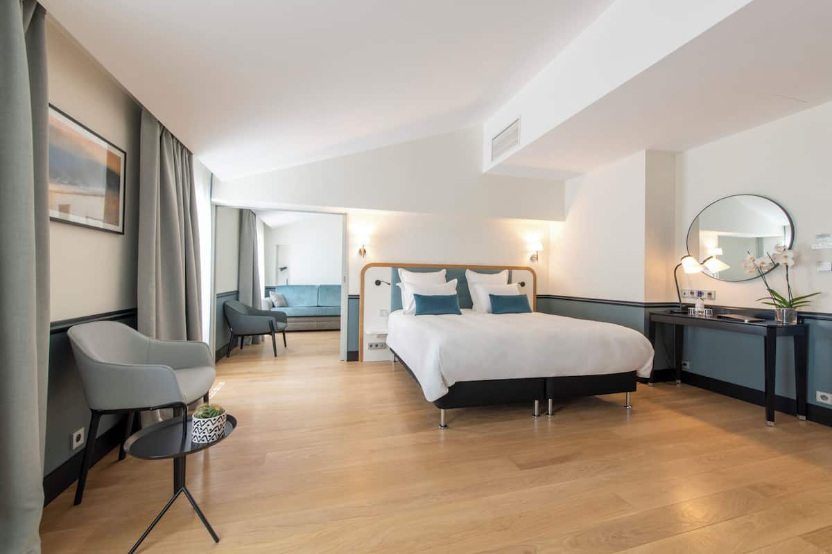 A modern hotel room with a bed, bedside table, chair, and a view of the sea.