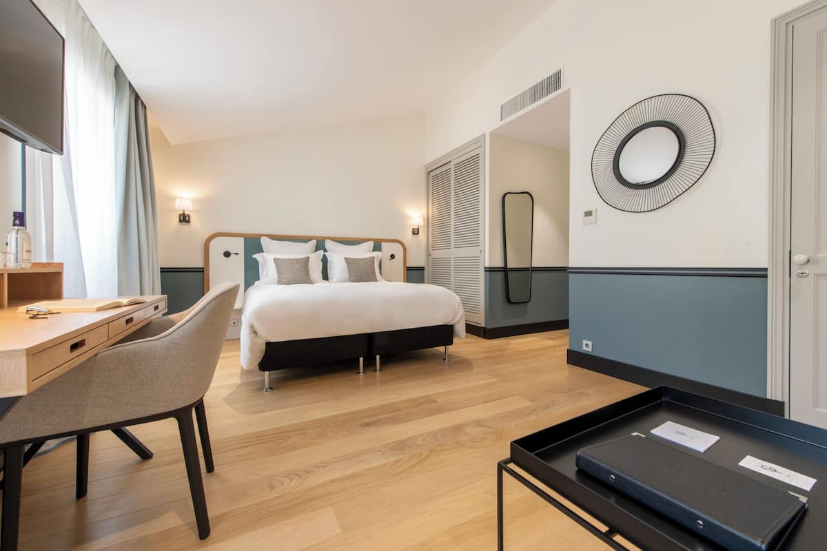 A hotel room with a bed, a desk, a chair, a mirror, and a tray with items on it.