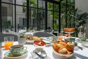 Un desayuno con una mesa dispuesta para dos personas, con cruasanes, pastelería y un bol de fruta.